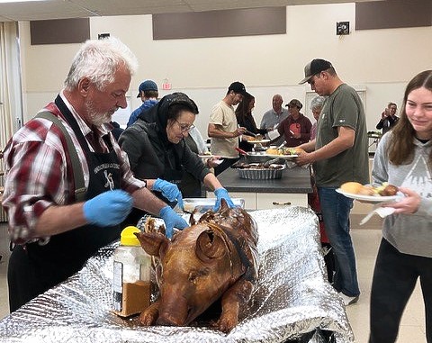 Image of a caterer carving roast pork while people go through a buffet line.