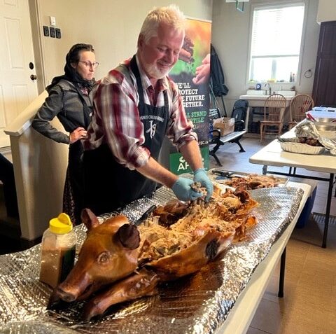 Image of a caterer removing meat from a roast hog.