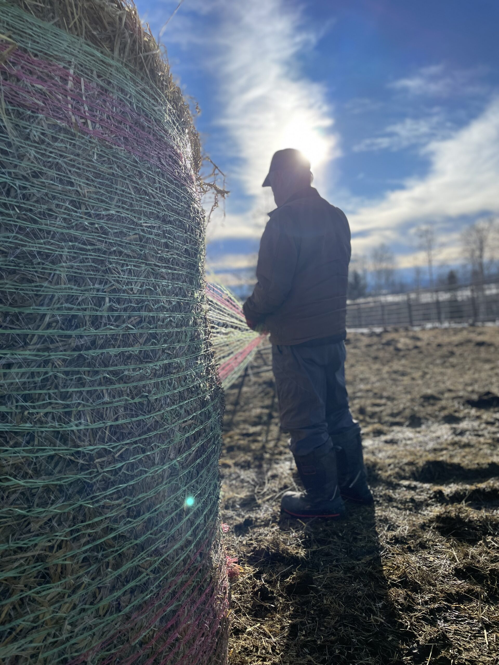 A producer, wearing chore boots, works with a round bale.