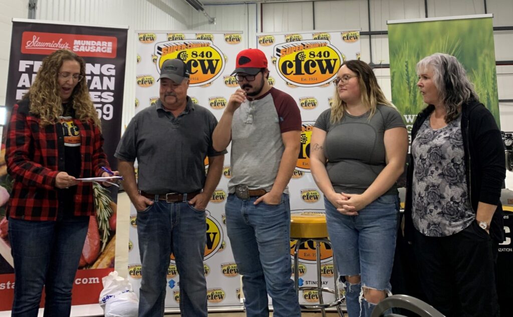 The Smerychunskis stand in front of a row of banners as they learn about their Meals in the Field prize pack.