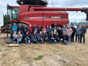 A group picture from week two of AFSC Farmer Feed north. The group is assembled in front of a red self-propelled combine.