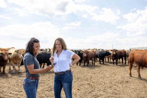 Two women in a corral in front of a group of cows