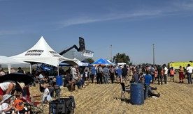People gather in a field for the Coaldale harvest. There are pop up tents in the background.