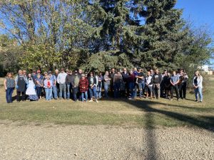 A group of people gathered for a photo in front of an evergreen and a deciduous tree.