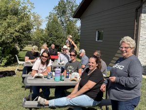 A group of people enjoy the sunshine while sitting on picnic tables.