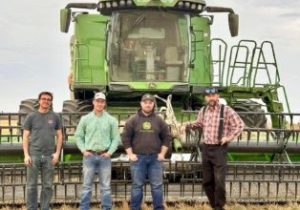 Four people stand in front of a green combine.