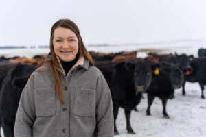 A woman stands in front of a herd of cattle in a snowy field