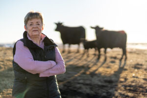 A woman stands in a field with two cows and a calf in the background