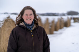 A woman stands in front of a row of snow-covered round bales