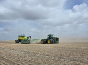 A green tractor pulls a green air seeder raising some dust in the field.
