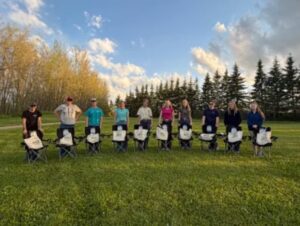 A group of youth pose with lawn chairs. They are standing on green grass.