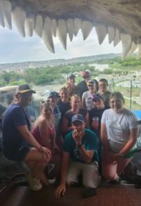 A group of youth pose for a picture. The top part of the frame is replica dinosaur teeth
