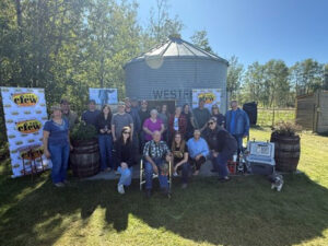A group of people pose in front of a round steel bin.